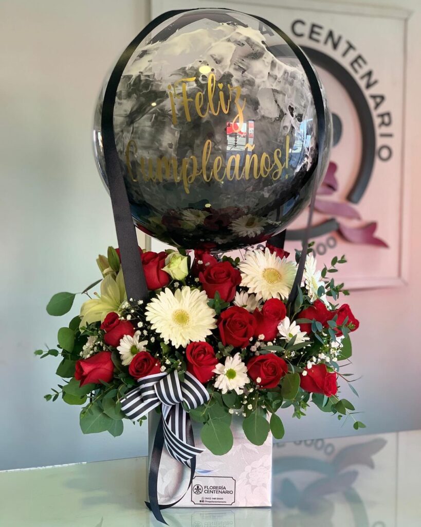 Arreglo con globo negro, base de rosas rojas y flores blancas.